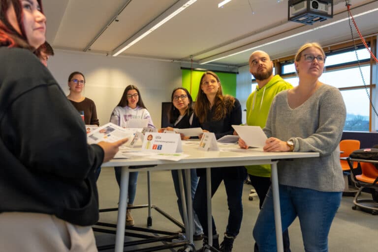 Eine Gruppe von Wissenschaftlern und Wissenschaftlerinnen des Instituts für nachhaltige Wassersysteme der Hochschule Hof (inwa) bei einer Besprechung. Sie stehen an einem Tisch und diskutieren Forschungsergebnisse. Das Bild zeigt das Engagement des Instituts für angewandte Forschung und den Wissenstransfer in die Praxis, mit einem Fokus auf Nachhaltigkeit und Digitalisierung.