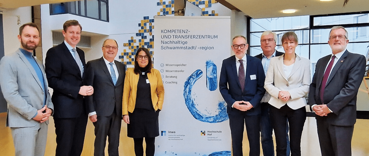 A group of representatives from the Institute for Sustainable Water Systems at Hof University of Applied Sciences (inwa) and partners pose in front of a banner of the Competence and Transfer Centre for Sustainable Sponge City/Region. The picture shows the cooperation and the focus on knowledge transfer, consulting and coaching in the field of sustainable water systems.