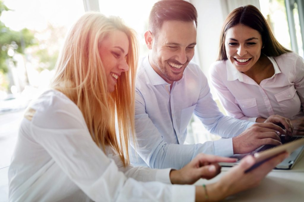 Eine Gruppe von drei jungen Fachleuten, die gemeinsam an einem Laptop und Tablet arbeiten und lachen. Das Bild symbolisiert die Innovationsberatung und -begleitung des Instituts für nachhaltige Wassersysteme der Hochschule Hof (inwa), die kreative Zusammenarbeit und Teamarbeit fördert.