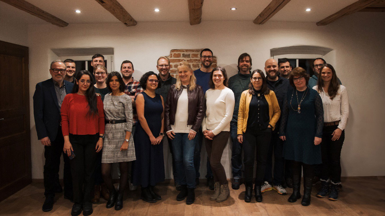 A group of employees from the Institute for Sustainable Water Systems at Hof University of Applied Sciences (inwa) pose in a room with wooden beams on the ceiling.